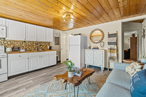 Cozy kitchen and living area with wooden ceiling, white cabinets, a sofa, and a decorative coffee table.